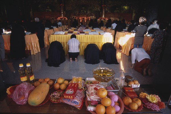 MALAYSIA, Penang, Kek Lok Si Temple, "Morning prayers in the main prayer hall. Kneeling worshippers with table in foreground spread with offerings of fruit, flowers and candles."