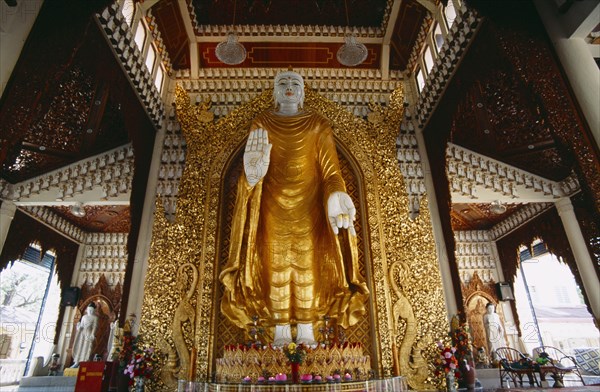 MALAYSIA, Penang, Georgetown, Dharmikarama Burmese Temple.  Interior with large standing Buddha figure with raised hand in gold painted robe and ornate carved gold panel behind.