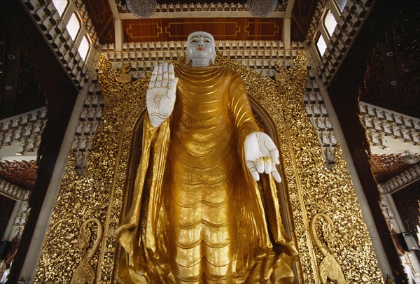 MALAYSIA, Penang, Georgetown, Dharmikarama Burmese Temple.  Interior with large standing Buddha figure with raised hand in gold painted robe and ornate carved gold panel behind.