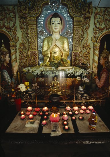 MALAYSIA, Penang, Georgetown, Dharmikarama Burmese Temple.  Interior with pink lotus flower shaped lighted candles in front of large seated Buddha and small golden Buddha figures.