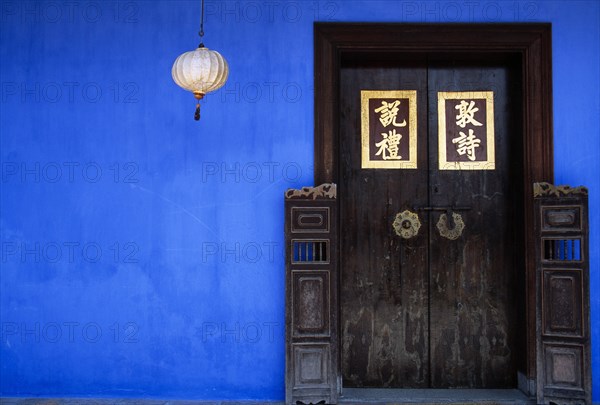 MALAYSIA, Penang, Georgetown, Cheong Fatt Tze Mansion.  Restored Chinese merchants house.  Wooden doorway with gold Chinese letters set into blue painted wall with lantern hanging at side.