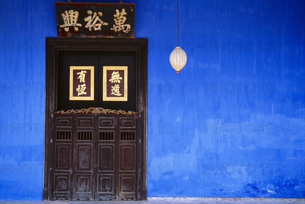 MALAYSIA, Penang, Georgetown, Cheong Fatt Tze Mansion.  Restored Chinese merchants house.  Wooden doorway with gold Chinese letters set into blue painted wall with lantern hanging at side.