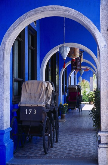 MALAYSIA, Penang, Georgetown, Cheong Fatt Tze Mansion. View through series of covered archways running along exterior of house framing old rickshaws and hanging Chinese lanterns.