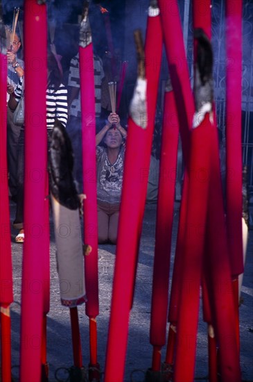 MALAYSIA, Penang, Georgetown, "Goddess of Mercy Temple, also known as Kuan Yin Teng.  Close view of large, pink burning sticks of incense with worshippers partly seen behind."