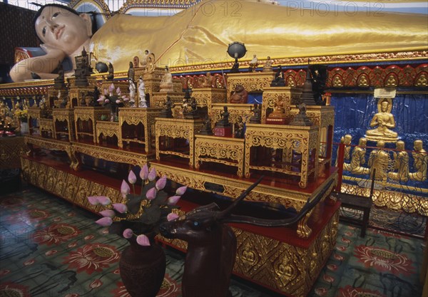 MALAYSIA, Penang, Georgetown, Wat Chayamangkalaram.  Interior with thirty-two metre long reclining Buddha lying behind display of various smaller figures and statues.