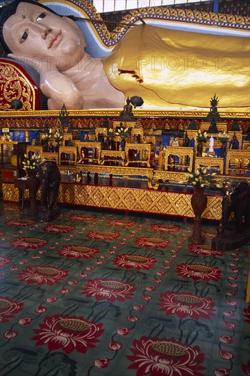 MALAYSIA, Penang, Georgetown, Wat Chayamangkalaram.  Interior with part view of 32 metre long reclining Buddha lying behind display of various smaller figures and statues.