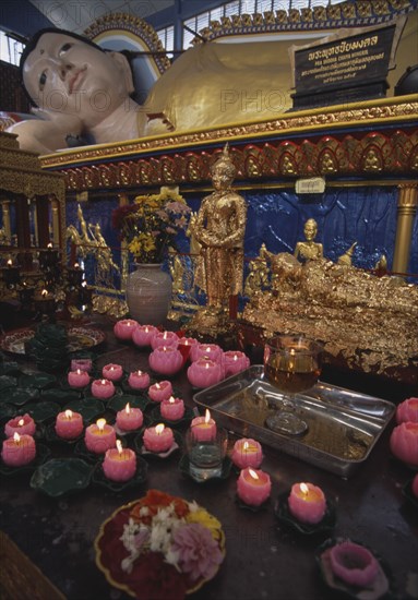 MALAYSIA, Penang, Georgetown, Wat Chayamangkalaram.  Interior.  Part view of  reclining Buddha lying behind smaller figures covered in gold leaf and lighted candles in the shape of lotus flowers.
