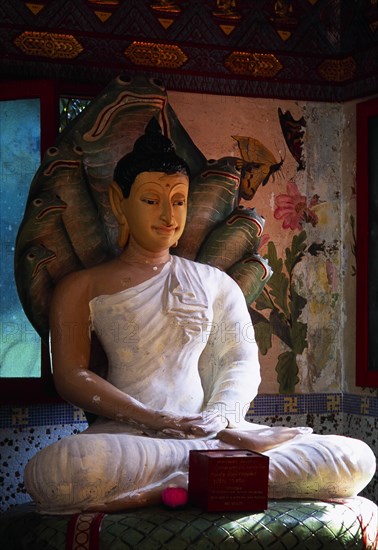 MALAYSIA, Penang, Georgetown, "Wat Chayamangkalaram.  Interior with seated Buddha figure in meditative pose on coiled naga with painted, multi headed hood."