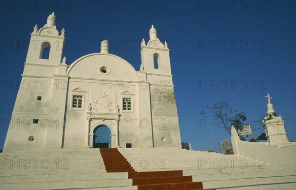 INDIA, Gujarat, Diu, Church of St Thomas. White painted exterior facade with painted red central strip leading up steps to blue door of entrance.