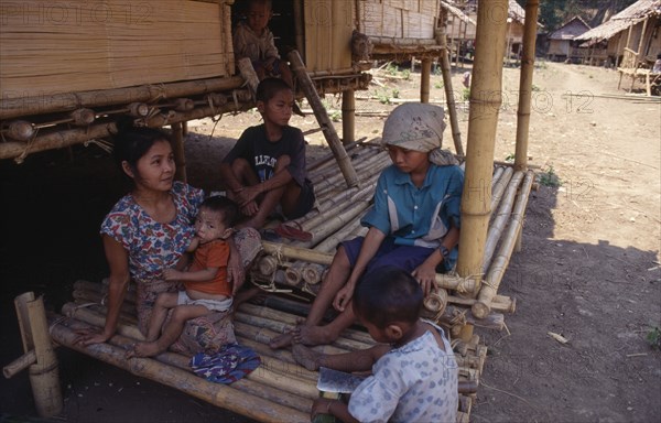THAILAND, North, Mae Sai , Karen refugee mother feeding child with four other children sitting in the shade