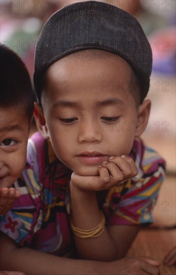 THAILAND, North, Mae Sai, Burmese Karen refugee child in camp looking down with his chin in his hand