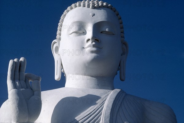 SRI LANKA, Mihinitale, White Buddha statue detail of head shoulders and hand against blue sky