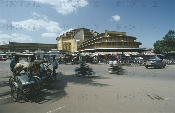 CAMBODIA, Phnom Penh, Trishaws and motorcyclists on road in front of the Central market buildings.