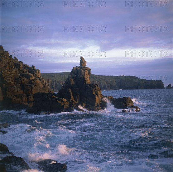 ENGLAND, Cornwall, Lands End, The Irish Lady stone stack below the cliffs with waves crashing against it in the evening light