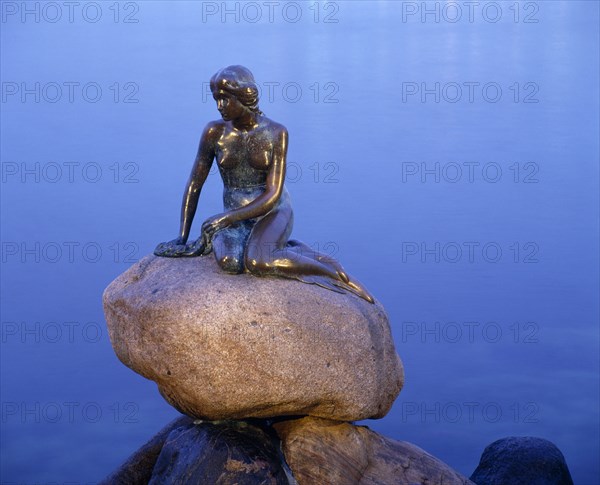 DENMARK, Zealand, Copenhagen, The Little Mermaid bronze statue seated on a rock at dusk with calm water