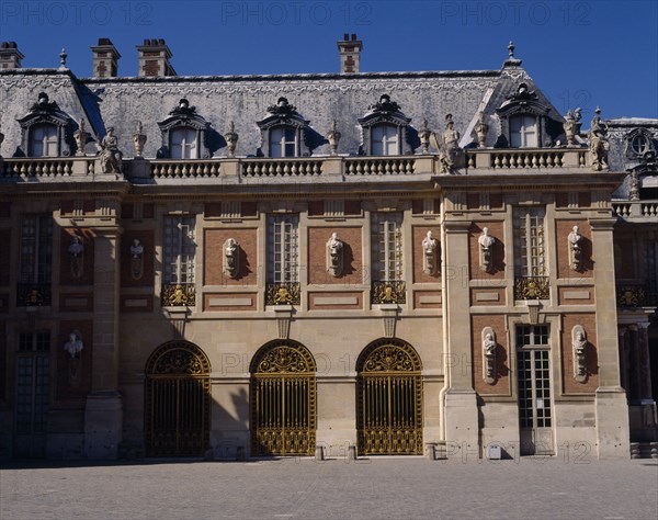 FRANCE, Ile de France, Yvelines, "Versailles. Part of palace with statues on walls, arches, balustraded roof and gravel in foreground"