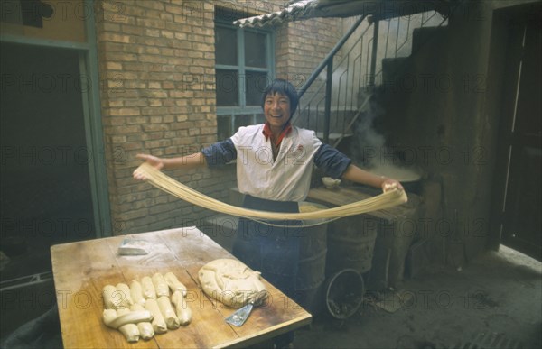 CHINA, Gansu Province, Lanzhou, "Smiling young man making noodles, holding long ribbons of dough in outstretched arms."
