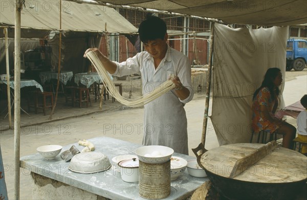 CHINA, Henan Province, Shaolin Monastery, Young man making noodles at food stall by swinging the dough into thin strips.