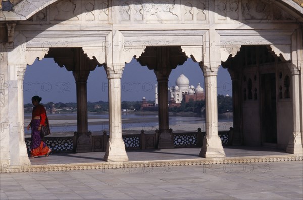 INDIA, Uttar Pradesh, Agra, "View towards the Taj Mahal seen through covered, colonnaded walkway with woman wearing red and purple sari on left hand side. "