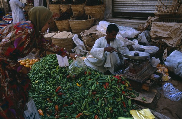 EGYPT, Upper Egypt, Luxor, Woman buying green chilli peppers in a street market with the vendor weighing some peppers