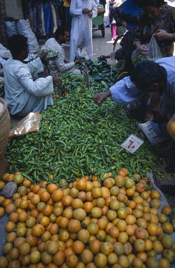 EGYPT, Upper Egypt, Luxor, Fruit and vegetable market with vendors and customers inspecting the produce of green chilli peppers and oranges