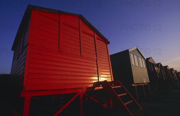 ENGLAND, Kent, Whitstable, Row of beach huts painted different colours on the beach in golden evening light