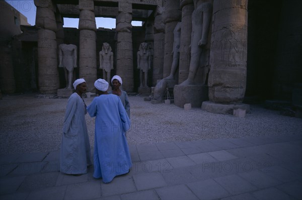 EGYPT, Upper Egypt, Luxor, Group of three men talking inside the temple of Luxor Statues in background