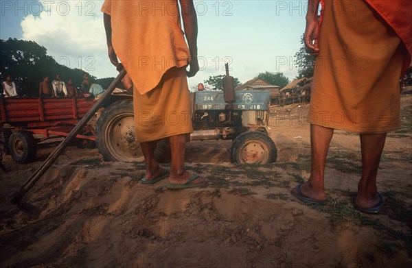 CAMBODIA, Kompong Thom, Building construction.  Cropped view of monks with hoe watching tractor and trailer.