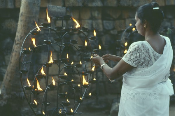 SRI LANKA, Anuradhapura, Lighting lamp beside Bo tree during Wesak festival.