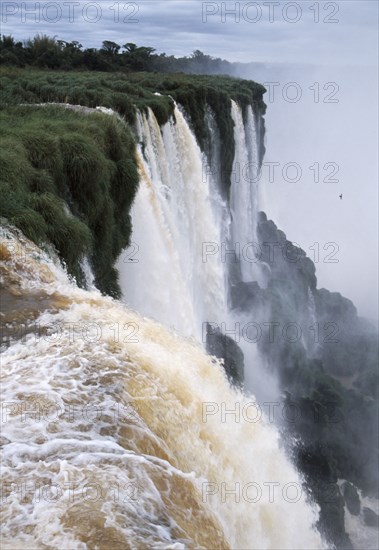 ARGENTINA, Misiones Province, Iguazu National Park, Iguazu Falls cascading over green cliffs.