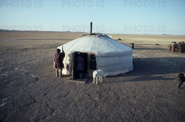 MONGOLIA, People, Ger or yurt in winter camp with dogs tied up outside and herdsman standing beside entrance.