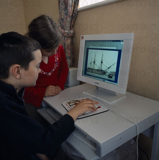 INDUSTRY, Computers, Children, Young boy and girl sitting at a home computer looking at educational web site with image of HMS Victory on the screen.