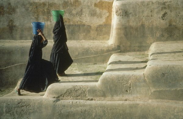 YEMEN, Shaharah, "Two veiled women fetching water carrying buckets on their heads, walking up steps from village cistern."