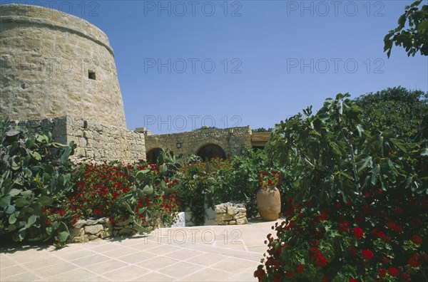 MALTA, Gozo, Ta’ Cenc, Entrance to Ta’ Cenc Hotel with traditional grain store and lined with flowers.