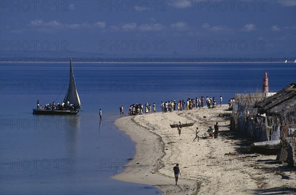 MOZAMBIQUE, Pemba, Fishing boat off the coast and waiting crowd of people on sandy beach with dilapidated thatched huts.
