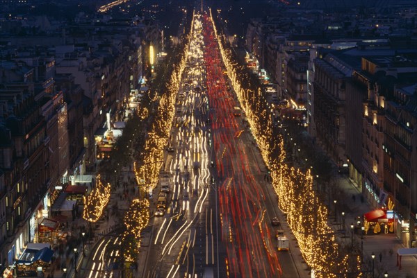 FRANCE, Ile de France, Paris, Les Champs Elysees at night with illuminated shop fronts and traffic light trails.