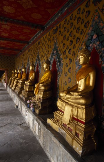 THAILAND, Bangkok Area, Bangkok, Wat Arun. Golden seated Buddha statues in cloister of Ordination Hall.
