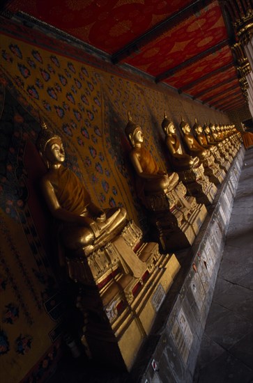 THAILAND, Bangkok Area, Bangkok, Wat Arun. Golden seated Buddha statues in cloister of Ordination Hall.