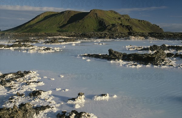 ICELAND, Gullbringu, Reykjanes Peninsula, Blue Lagoon at Svartsengi geo thermal power station.  Hot blue water with mineral deposits and mountain backdrop.