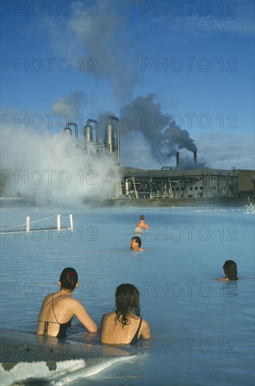 ICELAND, Gullbringu, Reykjanes Peninsula, Blue Lagoon at Svartsengi geo thermal power station. Bathers in the steaming blue water with power plant beyond.