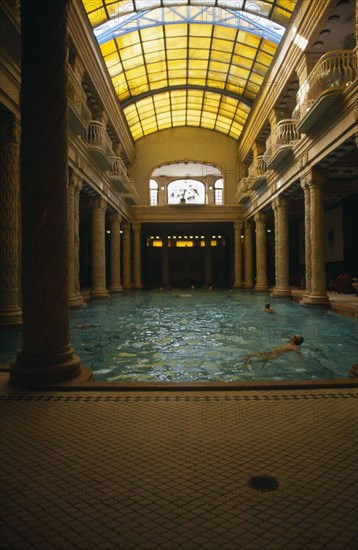 HUNGARY, Budapest, Gellert Baths.  Interior with bathers in swimming pool lined with carved pillars and with domed glass roof above.