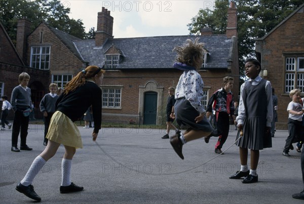 ENGLAND, Birmingham, Primary schoolchildren playing skipping games in playground.