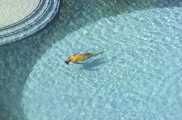 WEST INDIES, Dutch Antilles, Aruba, Aerial view looking down on clear blue swimming pool with single female bather in a yellow swimsuit.