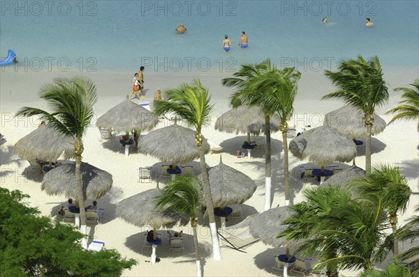WEST INDIES, Dutch Antilles, Aruba, View looking down on golden sandy beach with thatched umbrellas and people walking along the waters edge