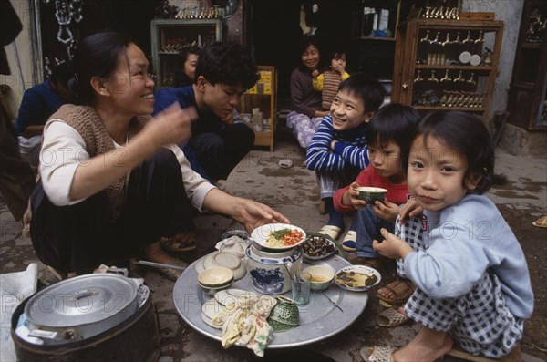 VIETNAM, North, Hanoi, Woman and children having a meal from a tray on the pavement outside their shop