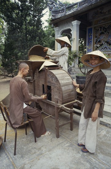 VIETNAM, Hue, Monks husking rice in a traditional hand driven machine