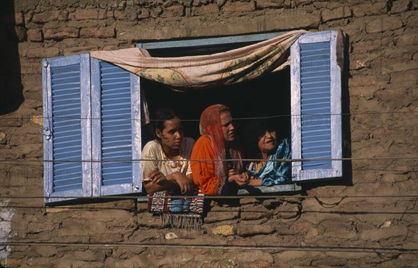 EGYPT, Nile Valley, Luxor, City housing with women at open window with blue and white wooden shutters.