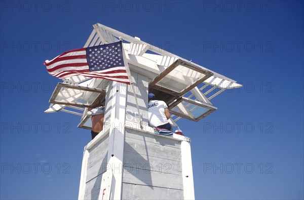 USA, Florida, Fort Lauderdale, Life Guard sitting on watch tower flying the stars and stripes flag