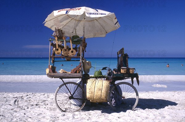 CUBA, Varadero, Beach vendors stall on a bycicle selling musical instruments and hats with clear blue sea beyond
