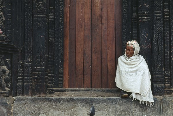 NEPAL, Bhaktapur, Man wrapped in white shawl sitting on the temple steps